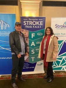Richard Crookes with wife Cathy standing in front of Stroke Banner detailing the "Stroke think FAST" message.